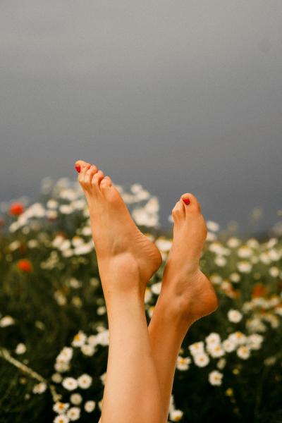 Ett par bara fötter i luften med blommor i bakgrunden och rött nagellack på tårna